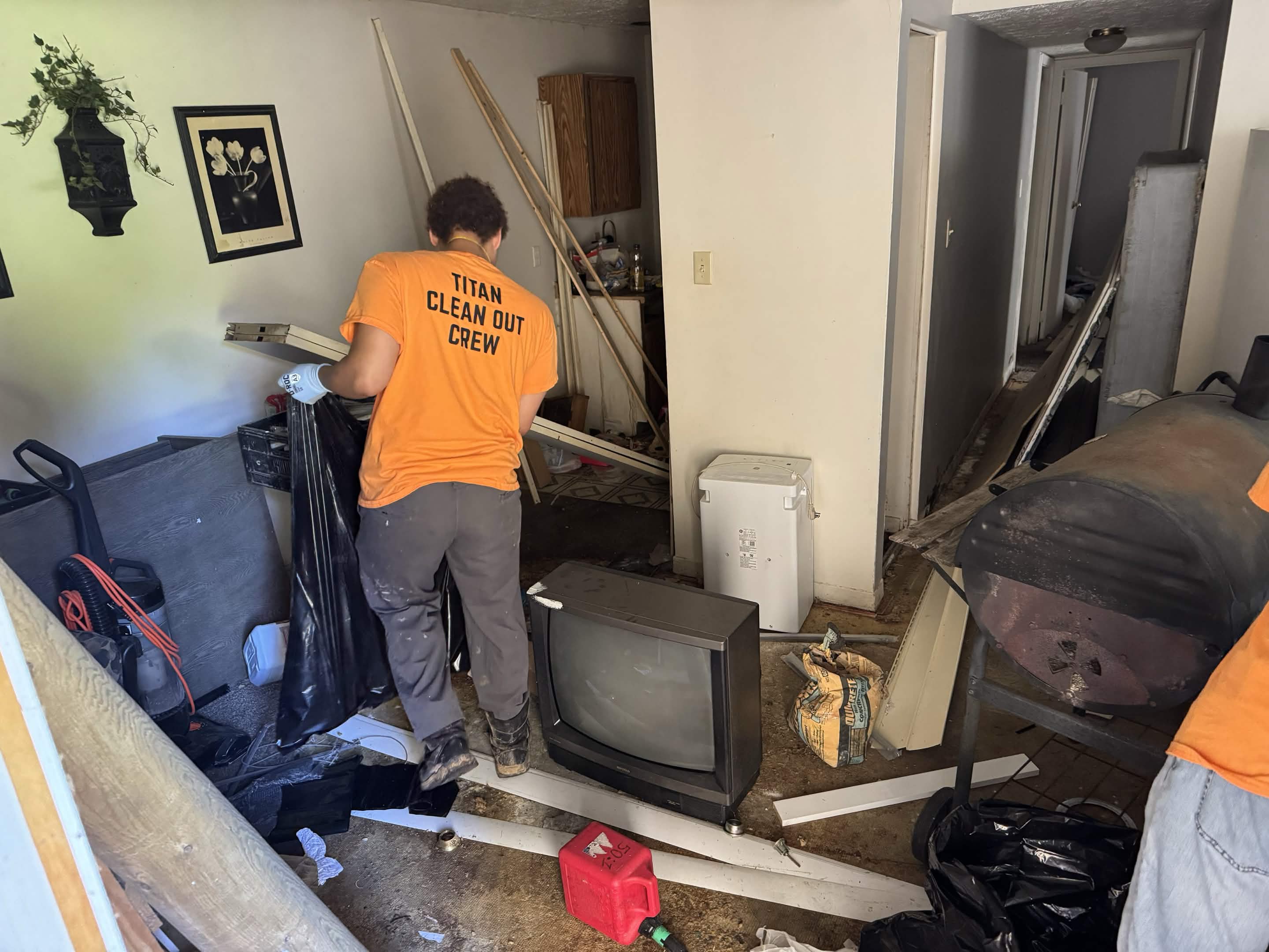 Titan clean-out crew member bagging debris while clearing a cluttered living room during a junk removal job