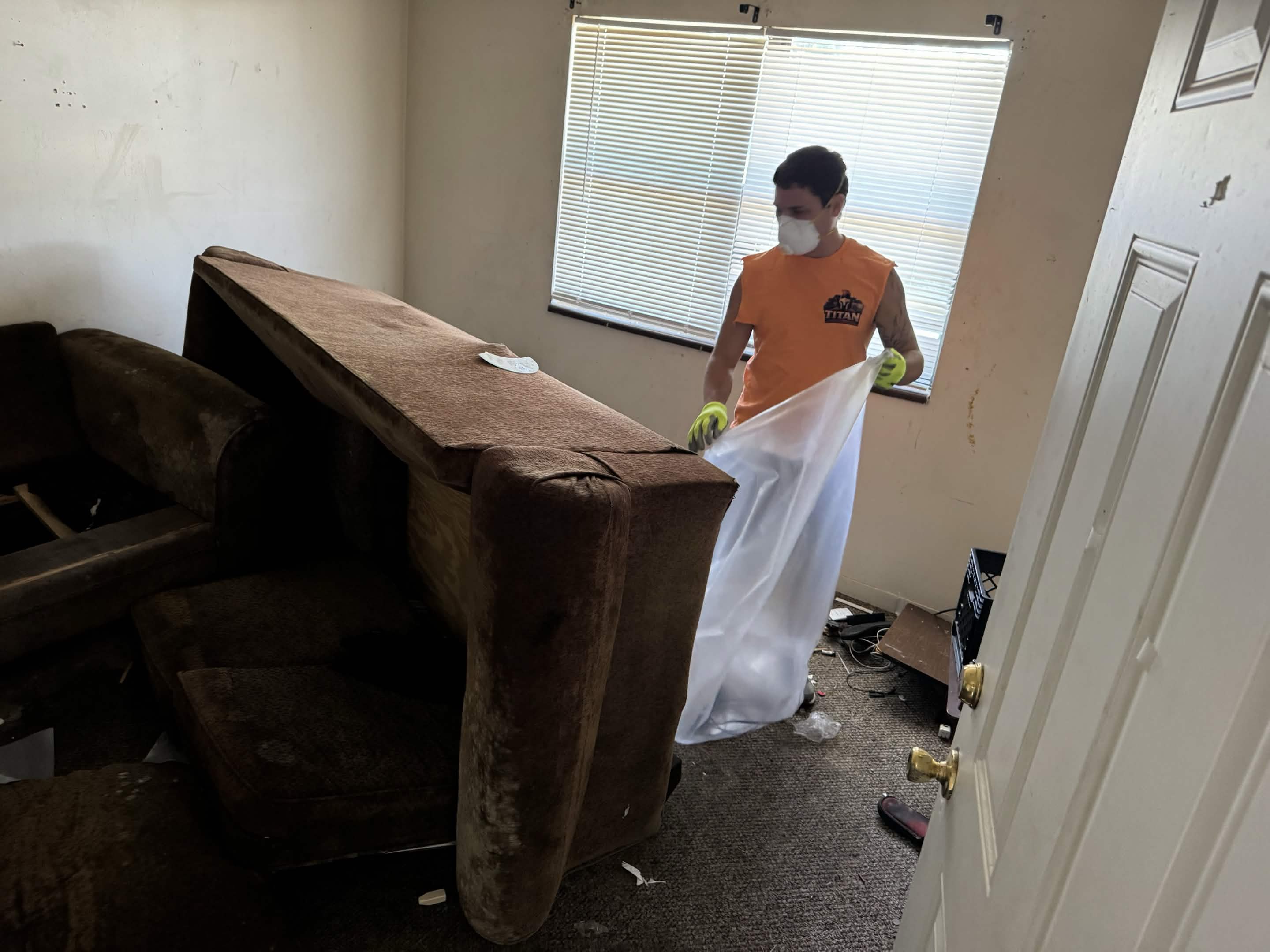 Titan Junk Removal crew member wrapping and hauling away an old couch during a furniture removal job